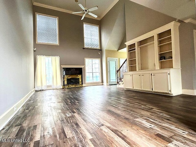 unfurnished living room with hardwood / wood-style floors, a stone fireplace, crown molding, ceiling fan, and a towering ceiling