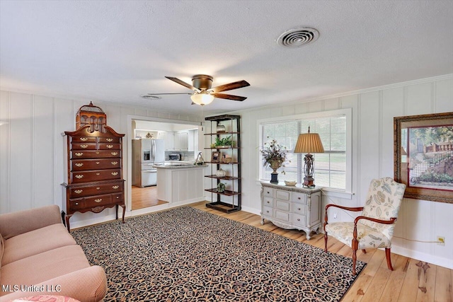 living room featuring ceiling fan, a textured ceiling, light hardwood / wood-style flooring, and ornamental molding