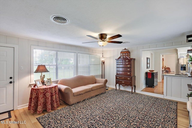 living room with ceiling fan, a textured ceiling, and light wood-type flooring