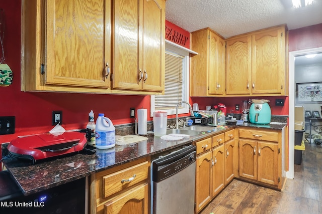 kitchen with sink, a textured ceiling, stainless steel dishwasher, dark stone counters, and light wood-type flooring