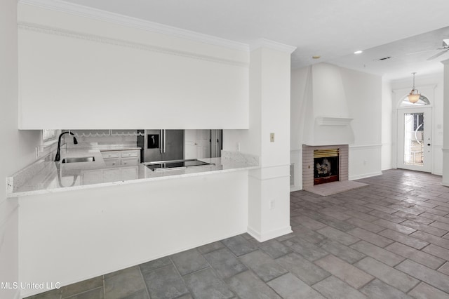 kitchen with light stone counters, black electric cooktop, a fireplace, a sink, and backsplash