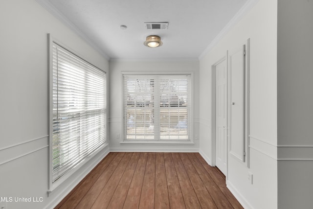 interior space with ornamental molding, wood-type flooring, visible vents, and baseboards