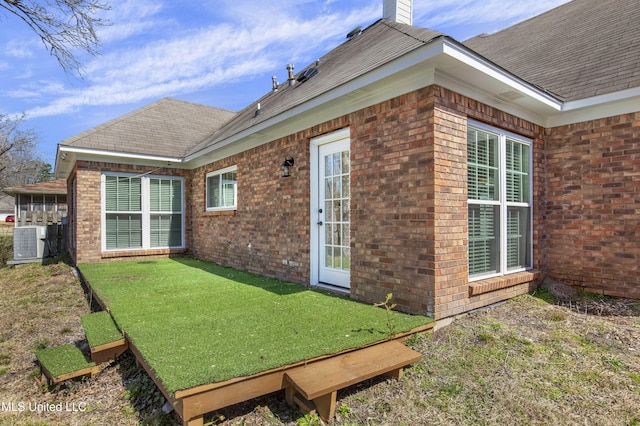 exterior space with cooling unit, brick siding, a yard, roof with shingles, and a chimney