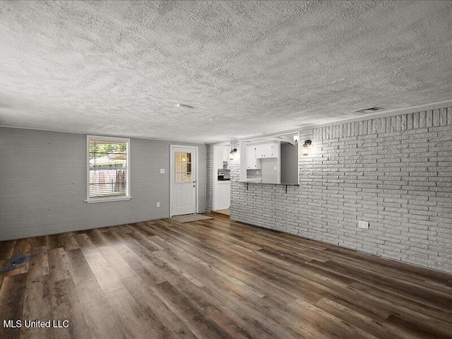 203 Barrow St, Pearl, MS 39208 - unfurnished living room featuring dark wood finished floors, a textured ceiling, and brick wall