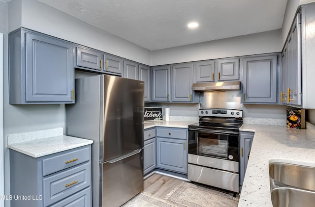 kitchen with stainless steel appliances, under cabinet range hood, gray cabinetry, a sink, and light wood-type flooring