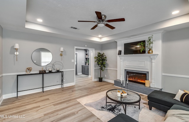 living area featuring a ceiling fan, wood finished floors, a fireplace, a tray ceiling, and baseboards