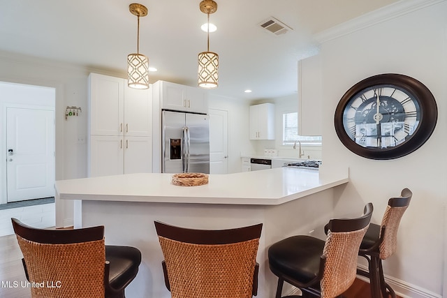 kitchen featuring white cabinets, a kitchen bar, stainless steel appliances, hanging light fixtures, and kitchen peninsula