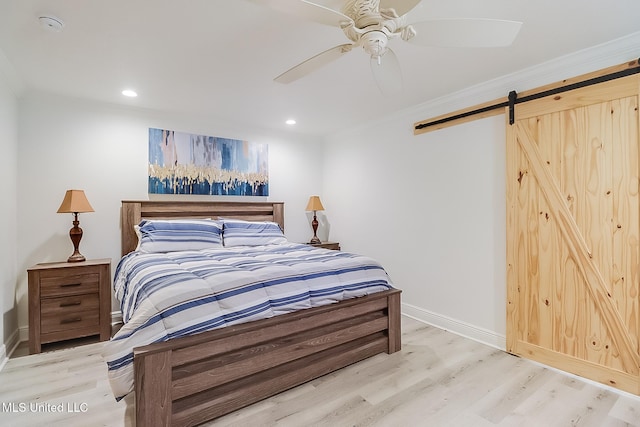 bedroom with ceiling fan, ornamental molding, a barn door, and light wood-type flooring