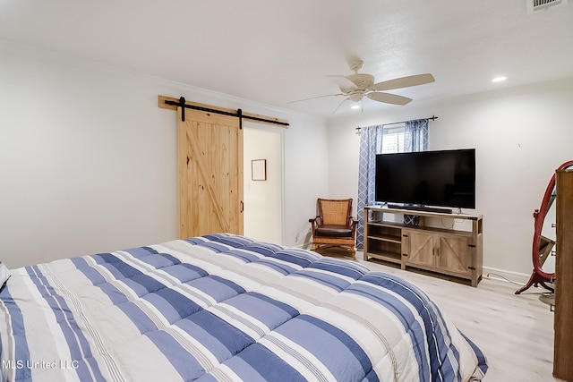 bedroom with ceiling fan, ornamental molding, a barn door, and light wood-type flooring