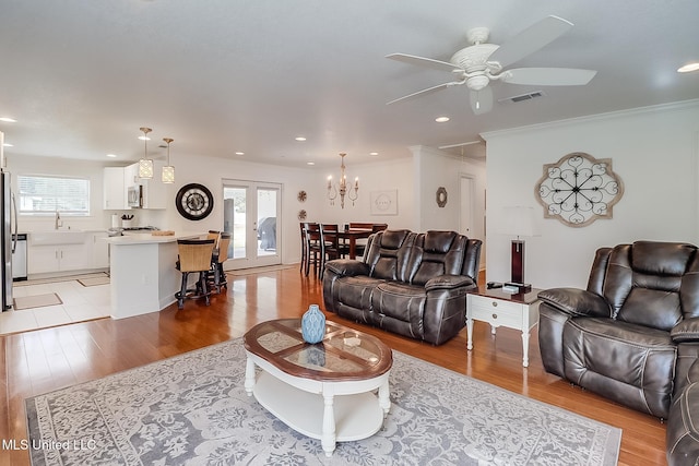 living room featuring ceiling fan, light hardwood / wood-style floors, sink, ornamental molding, and french doors