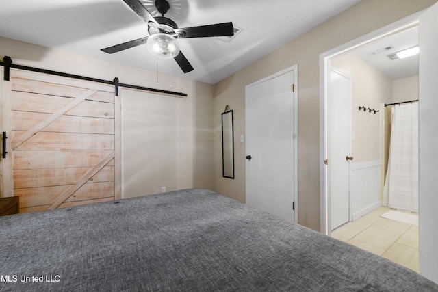 unfurnished bedroom featuring ceiling fan, ensuite bath, and a barn door