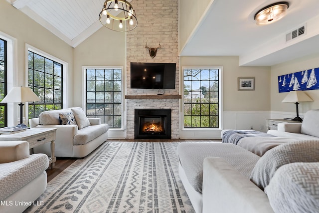 living room with a brick fireplace, an inviting chandelier, vaulted ceiling, and hardwood / wood-style flooring