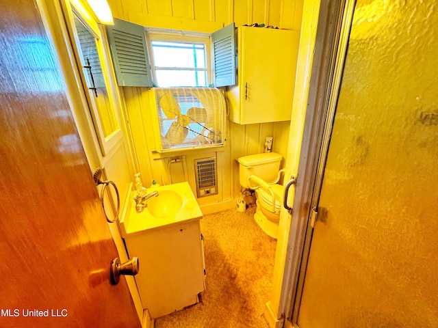 bathroom with vanity, toilet, wooden walls, heating unit, and a shower with shower door