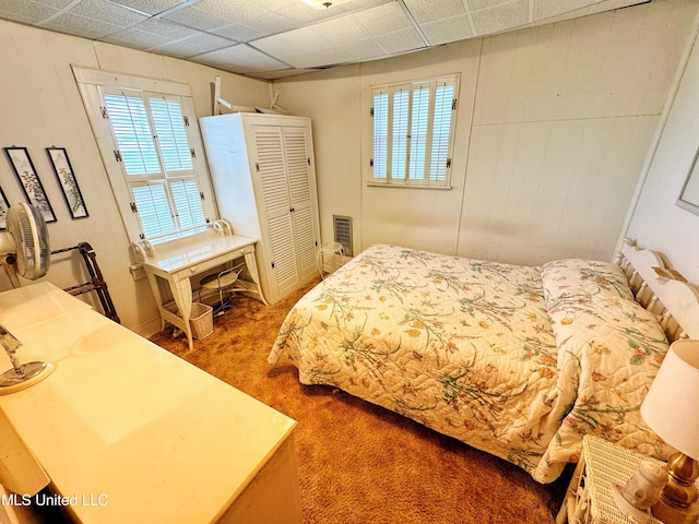 bedroom featuring carpet floors, a drop ceiling, and wooden walls