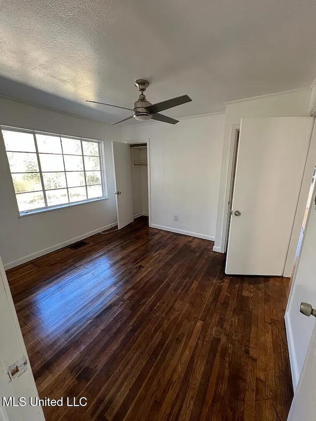 unfurnished bedroom with a textured ceiling, ceiling fan, dark wood-type flooring, and a closet