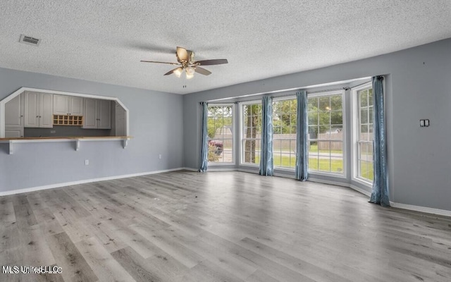 unfurnished living room featuring ceiling fan, light wood-type flooring, and a textured ceiling