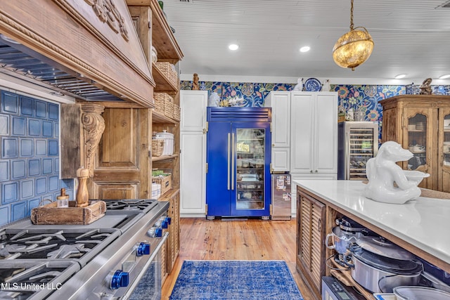 kitchen with premium appliances, light countertops, hanging light fixtures, white cabinets, and wallpapered walls