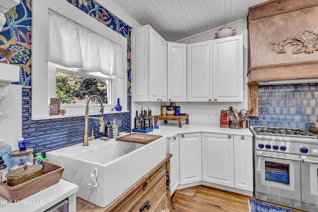 kitchen with white cabinets, light countertops, light wood-style floors, double oven range, and a sink