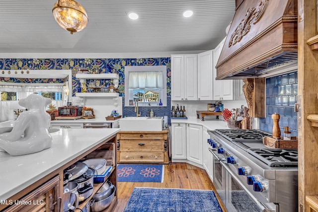 kitchen with light countertops, a sink, white cabinetry, and double oven range