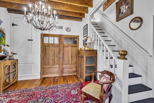 entryway with visible vents, stairway, an inviting chandelier, wood finished floors, and beamed ceiling