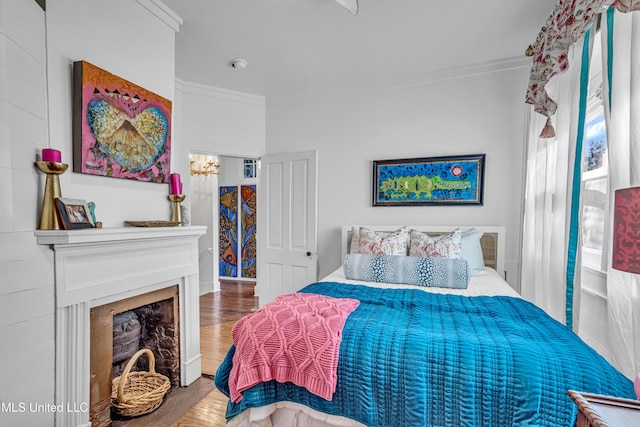 bedroom featuring a chandelier, a fireplace, crown molding, and wood finished floors