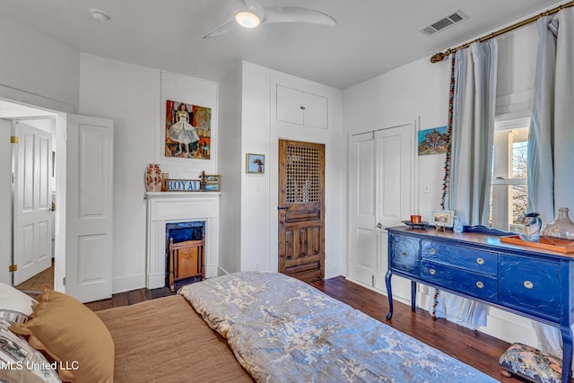 bedroom with visible vents, dark wood finished floors, ceiling fan, a closet, and a high end fireplace