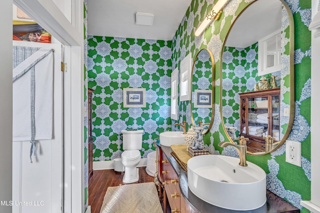 bathroom featuring wood finished floors, a sink, toilet, and wallpapered walls