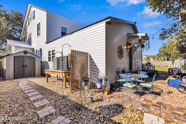 back of property with an outbuilding, a storage shed, central AC unit, a patio area, and fence