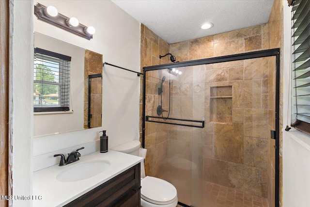 bathroom featuring toilet, a textured ceiling, vanity, and a shower with door