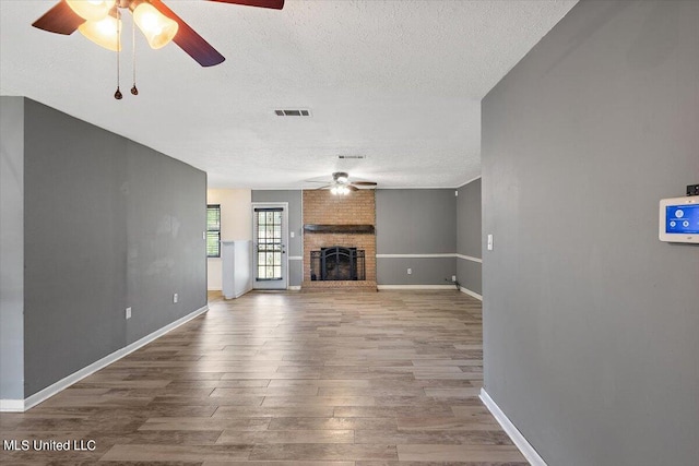 unfurnished living room with a textured ceiling, wood-type flooring, a fireplace, and ceiling fan