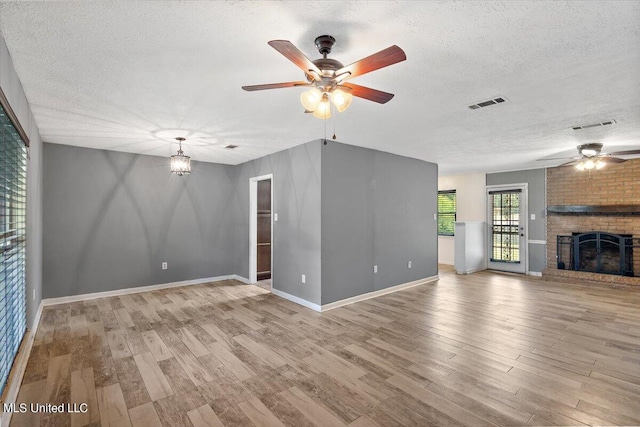 unfurnished living room featuring a fireplace, a textured ceiling, light wood-type flooring, and ceiling fan