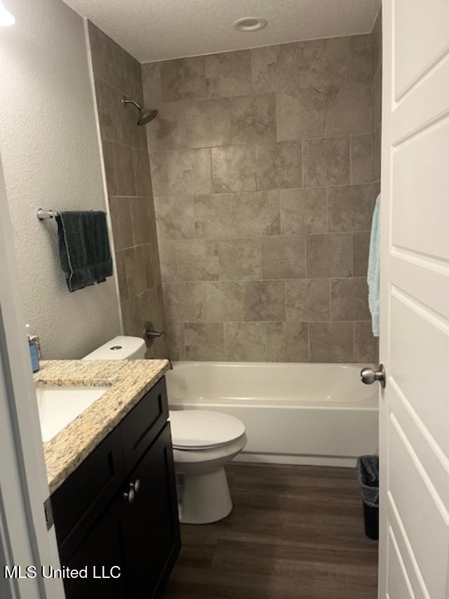 full bath featuring wood finished floors, shower / bathtub combination, vanity, toilet, and a textured ceiling