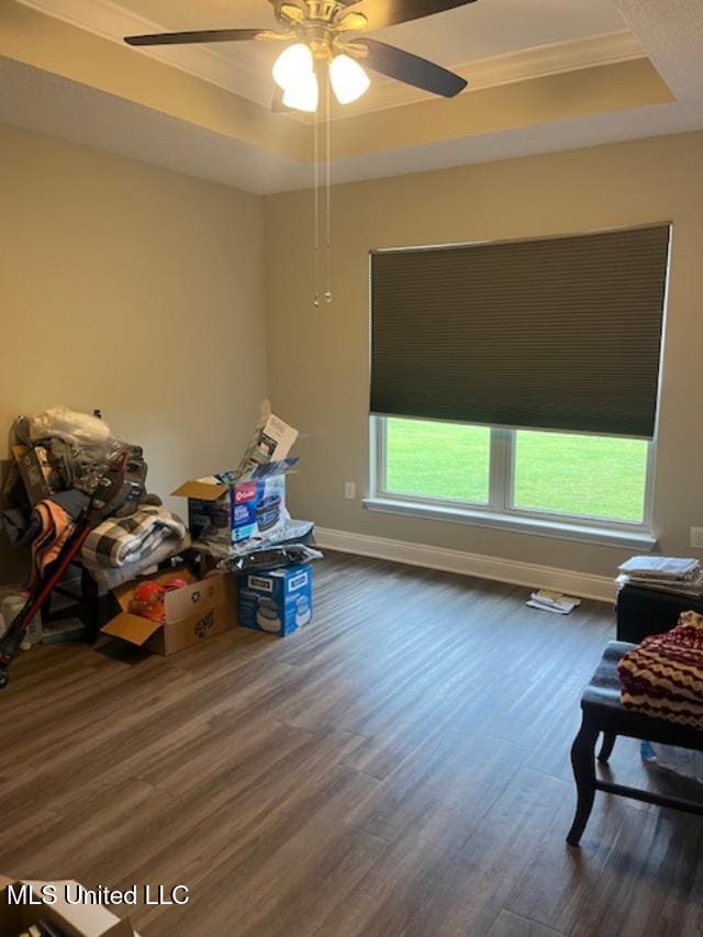bedroom featuring a tray ceiling, dark wood finished floors, ornamental molding, baseboards, and a ceiling fan