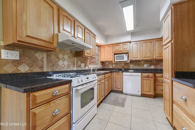 kitchen with white appliances, sink, backsplash, dark stone counters, and light tile patterned floors