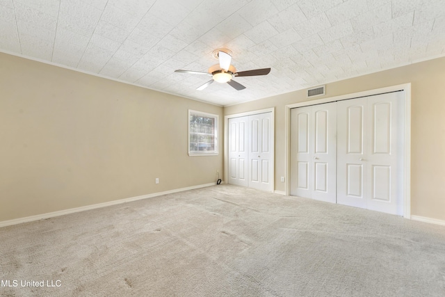 unfurnished bedroom with ceiling fan, visible vents, baseboards, carpet floors, and two closets