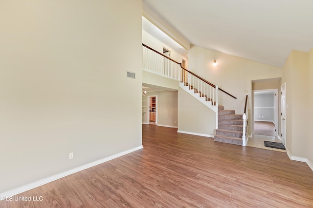 unfurnished living room featuring wood finished floors, stairway, baseboards, visible vents, and high vaulted ceiling
