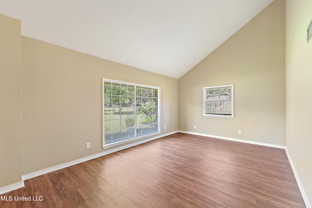spare room featuring wood finished floors, high vaulted ceiling, and baseboards