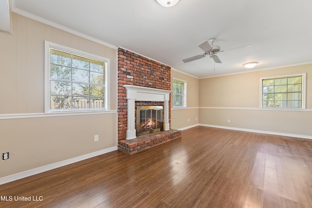 unfurnished living room featuring baseboards, ornamental molding, a brick fireplace, wood finished floors, and a ceiling fan