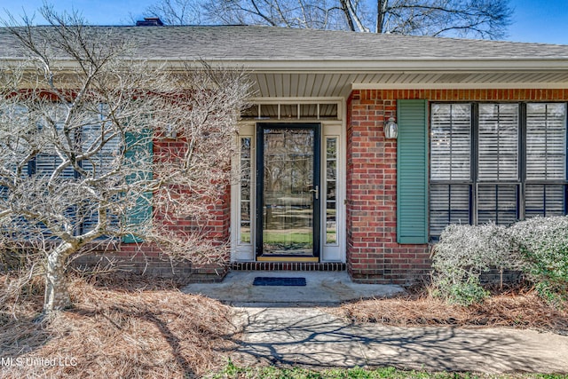 property entrance featuring a shingled roof and brick siding