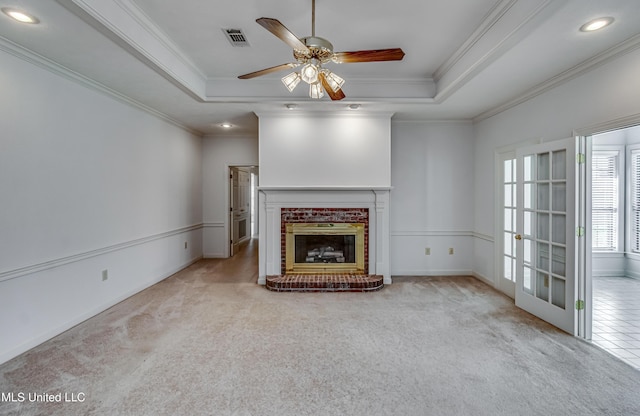 unfurnished living room featuring visible vents, carpet, a tray ceiling, crown molding, and a brick fireplace