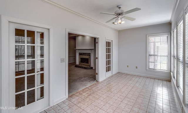 spare room featuring baseboards, a fireplace with raised hearth, a ceiling fan, light colored carpet, and ornamental molding