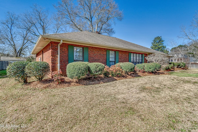 view of front facade with roof with shingles, a front yard, fence, and brick siding