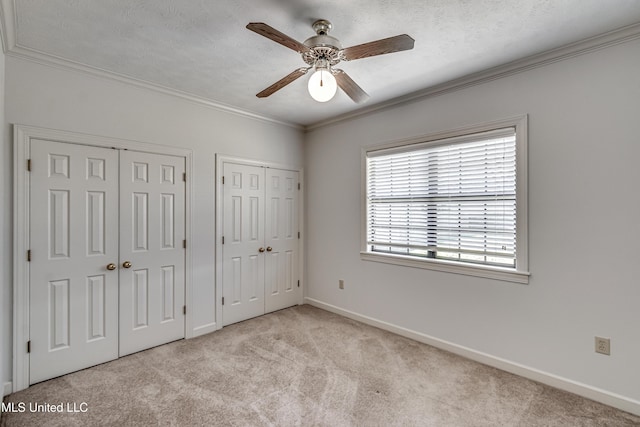 unfurnished bedroom featuring baseboards, light colored carpet, ornamental molding, a textured ceiling, and two closets