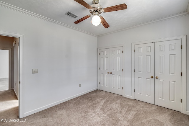 unfurnished bedroom featuring ornamental molding, carpet, visible vents, and multiple closets