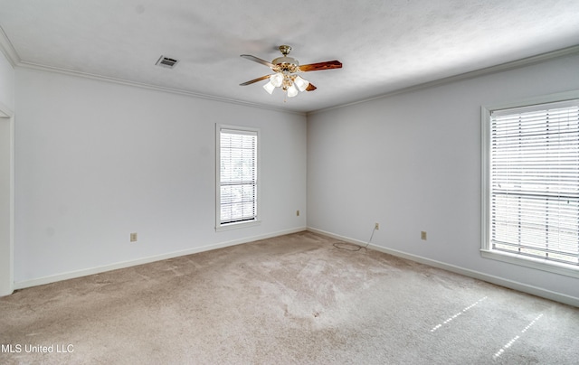 carpeted spare room with ornamental molding, visible vents, ceiling fan, and baseboards