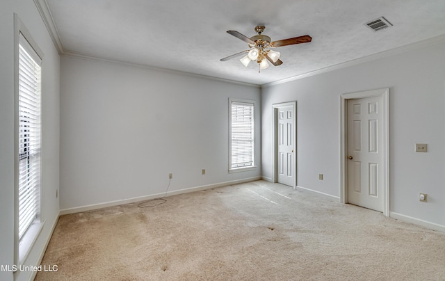 empty room with ceiling fan, light carpet, visible vents, baseboards, and crown molding