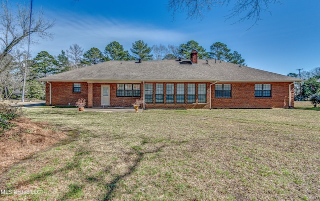 rear view of property with a lawn, a patio, a chimney, roof with shingles, and brick siding