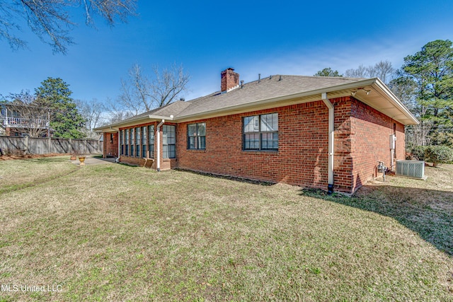 rear view of house featuring a chimney, fence, a yard, central air condition unit, and brick siding