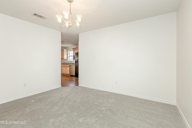 empty room with a textured ceiling, sink, light carpet, and a chandelier