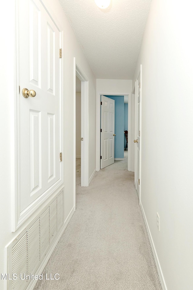 corridor with light colored carpet and a textured ceiling